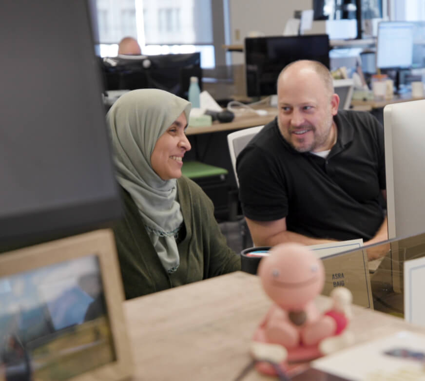 A man and a woman smiling and working together in front of computers